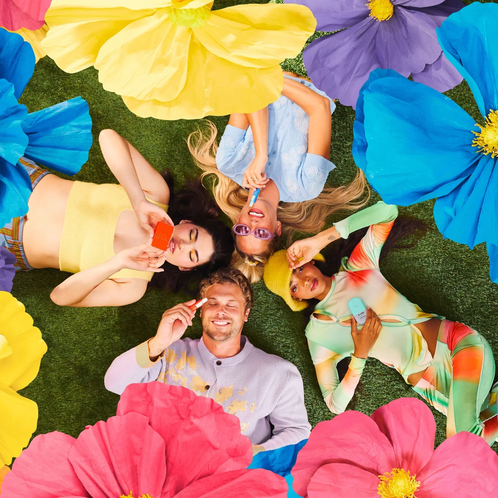People lying on grass with Wizard Wellness products surrounded by large colorful flowers