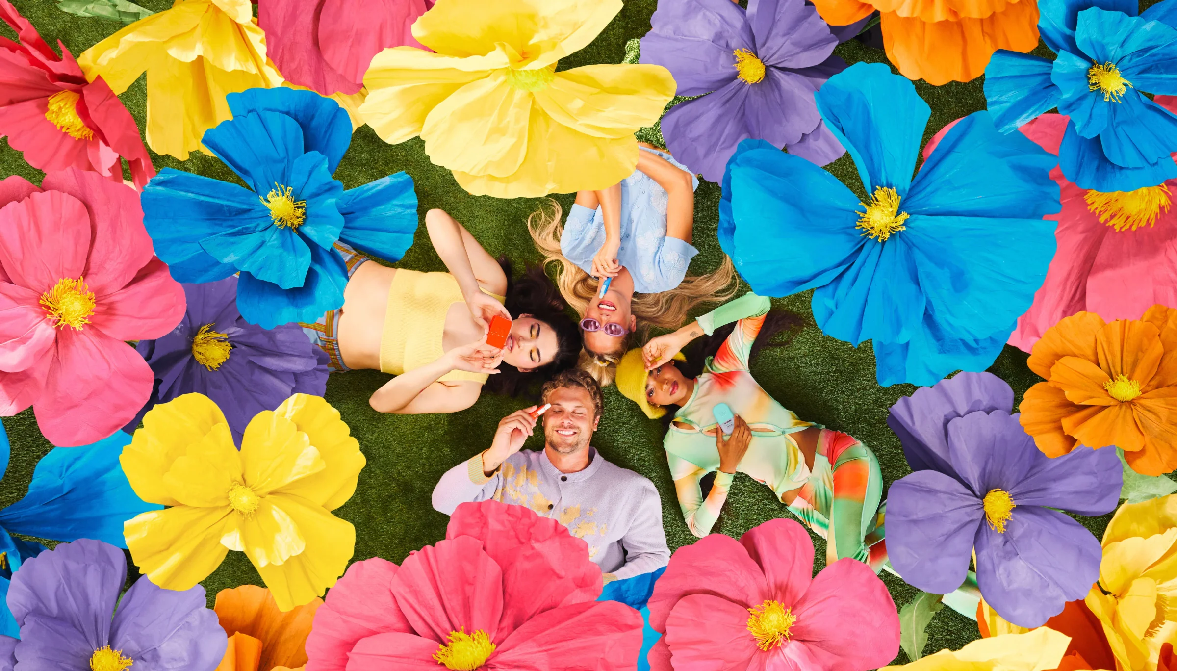 People lying on grass with Wizard Wellness products surrounded by large colorful flowers